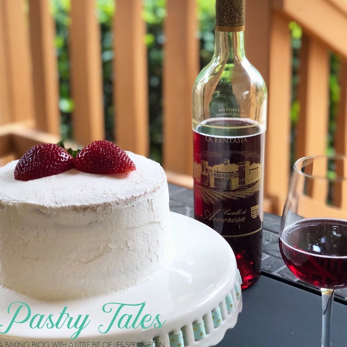 Cake with strawberries, red wine bottle, and wine glass on a table outdoors.