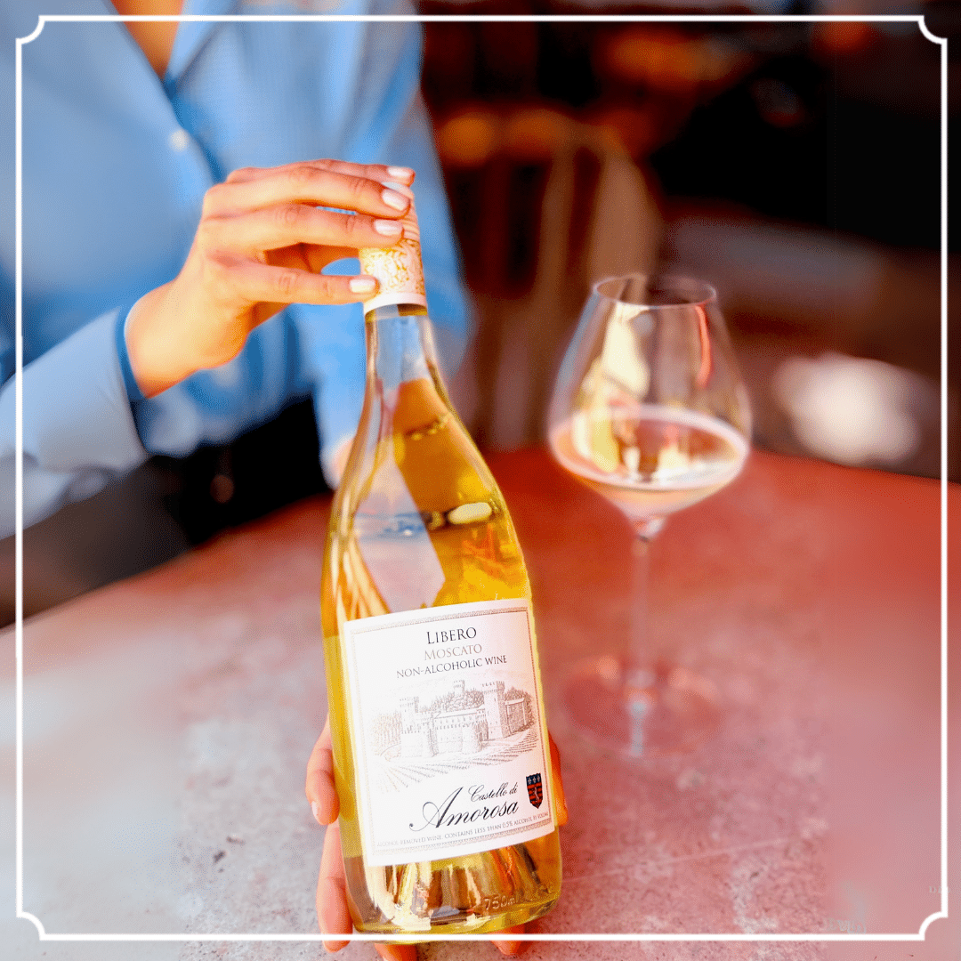 Person holding a bottle of wine with a glass on a table.