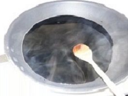 A pot of dark liquid simmering with a wooden spoon inside; steam rises.