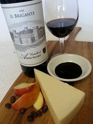 Wine, cheese, fruit, and balsamic glaze on a wooden board.