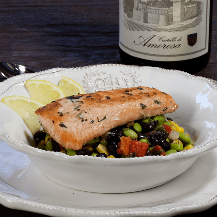 Grilled salmon on black bean and corn salsa, lemon wedges, wine bottle in background.