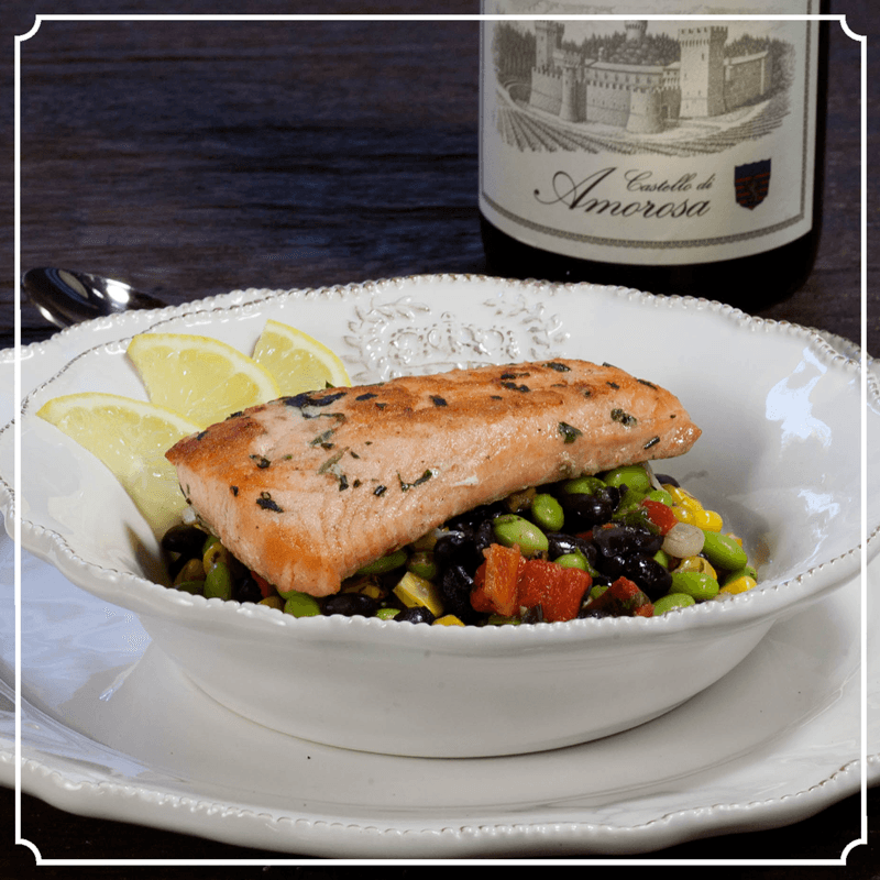 Salmon dish with vegetables and lemon, served in a bowl, with a wine bottle in the background.