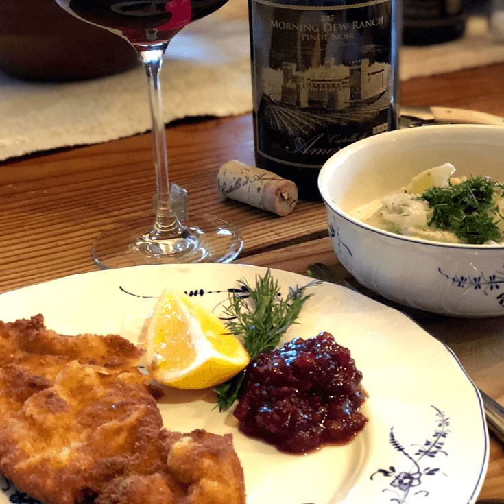 Plate with schnitzel, cranberry sauce, lemon, and wine with a bowl of food.