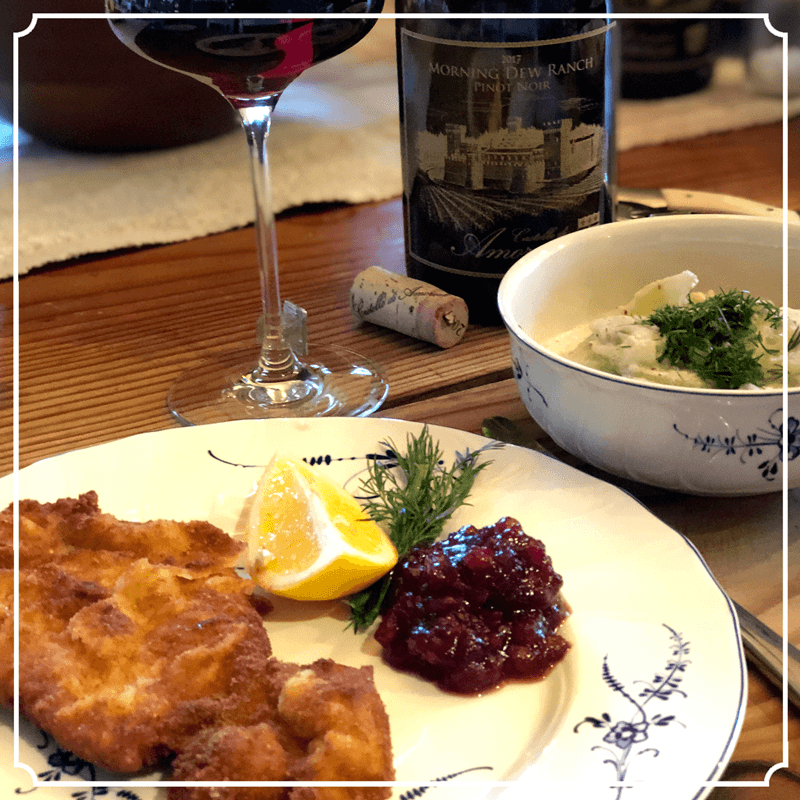 Plate of fried food, cranberry sauce, lemon, soup, wine, and bottle on a wooden table.