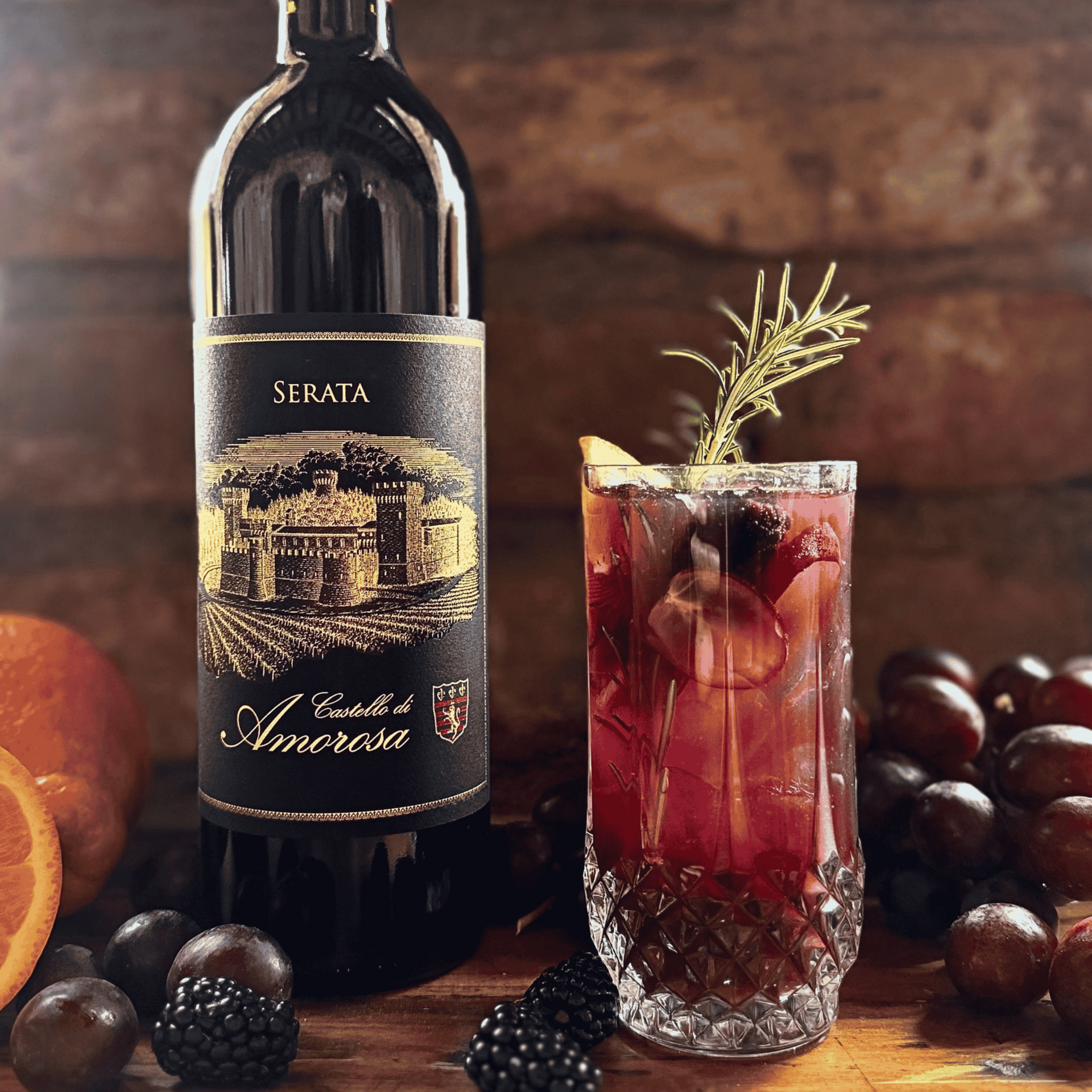 Wine bottle beside a ruby cocktail with citrus, berries, and grapes on a rustic wooden table