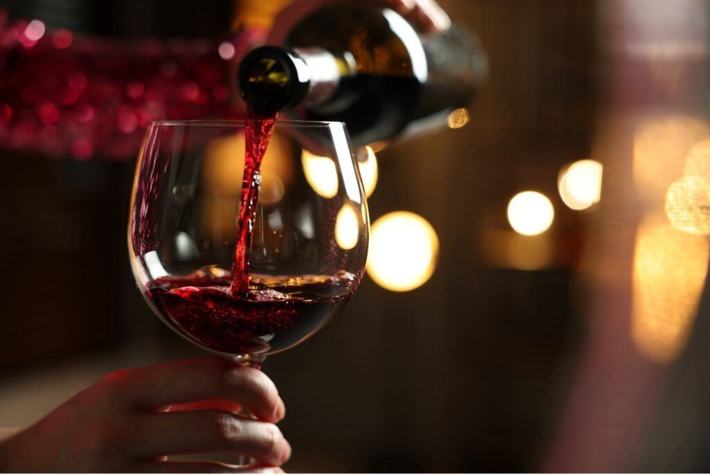 Red wine being poured into a glass, blurred background with lights.