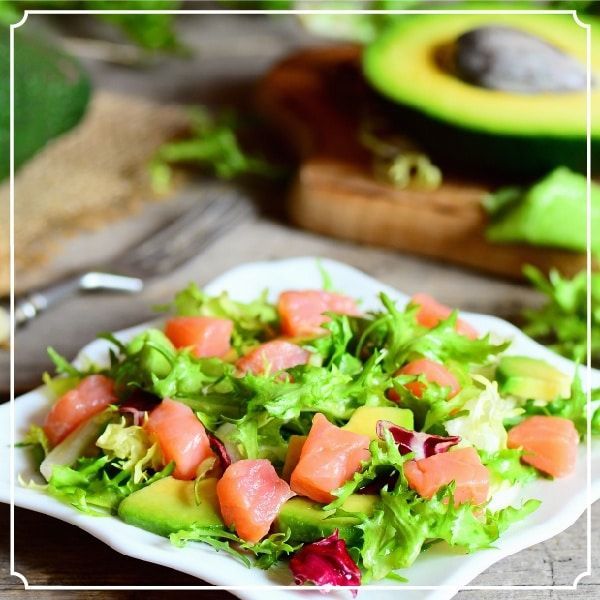 Salmon and avocado salad on a white plate with mixed greens.