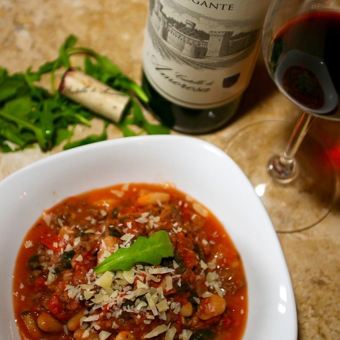 Bowl of soup with wine, greenery, and a wine bottle on a table.