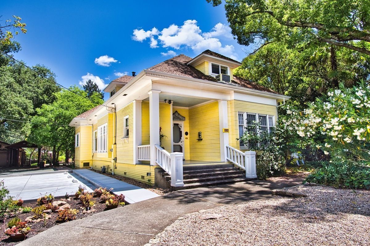 Yellow Victorian home with white porch and stairs surrounded by trees