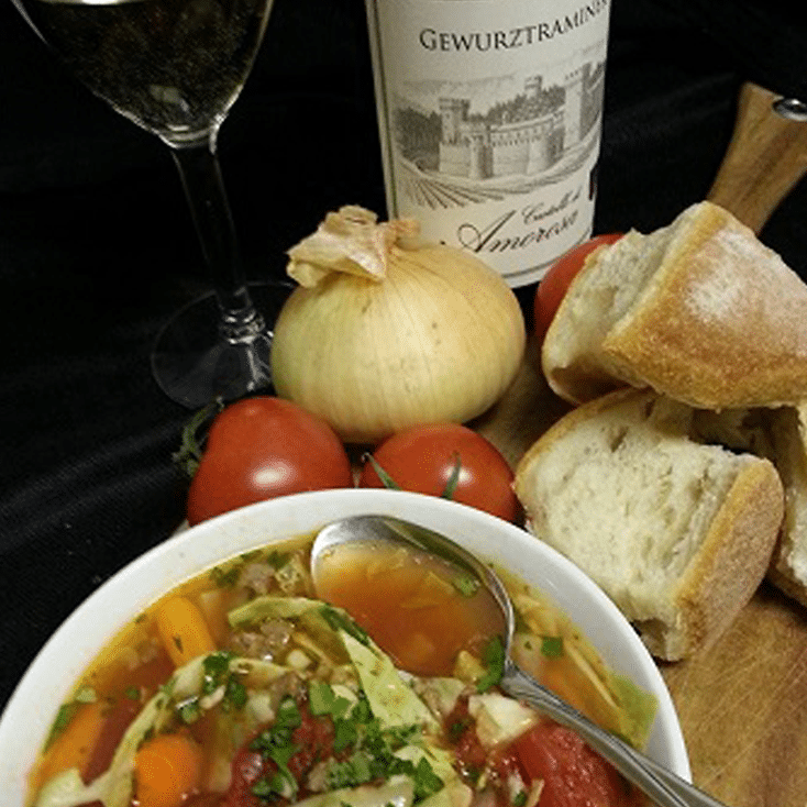 Bowl of soup with vegetables, bread, wine glass, tomatoes, and onion.