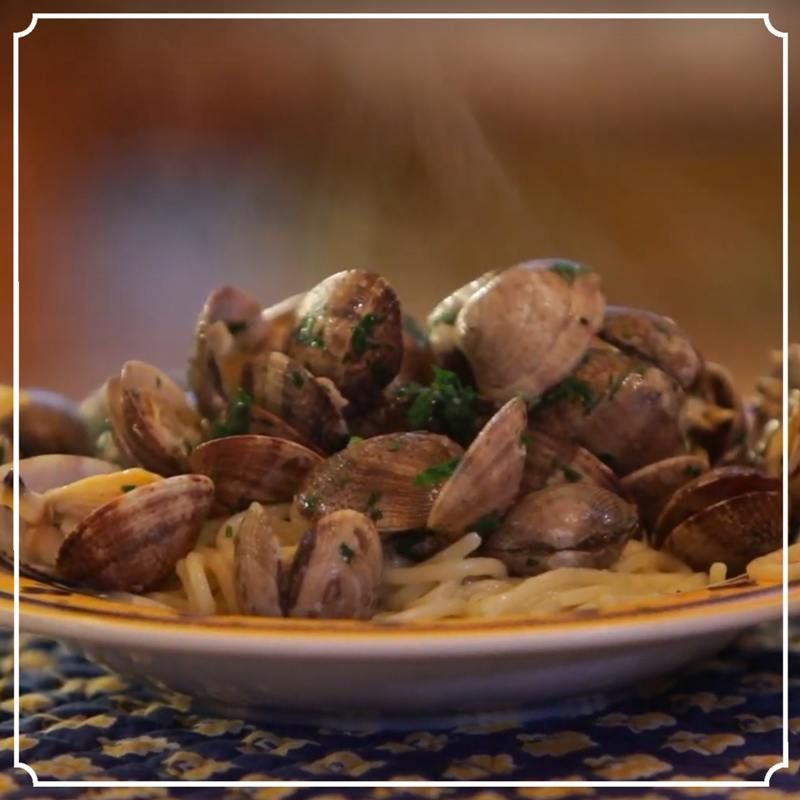Clams with parsley served atop spaghetti on a plate, steam rising.