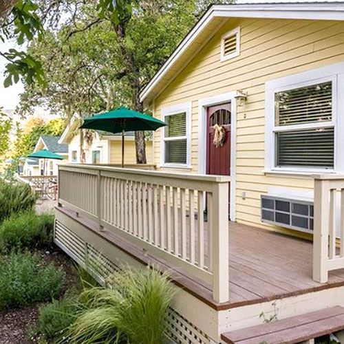 Yellow cabin with a porch, green umbrella, and a red door.