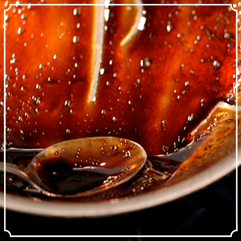 Spoon scooping up brown, glossy sauce from a dish; close-up with glistening surface.