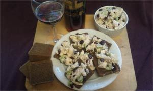 Chicken salad on rye bread, wine, and a bowl of salad on a wooden board.