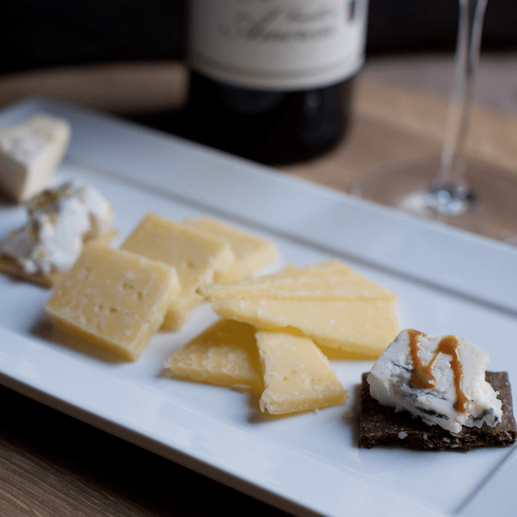 Cheese and crackers on a white platter, wine bottle, and a glass.