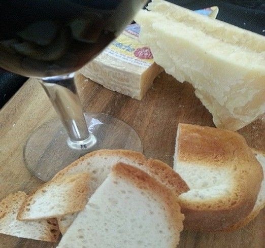 Wine glass with red wine, cheese, and toasted bread on wooden board