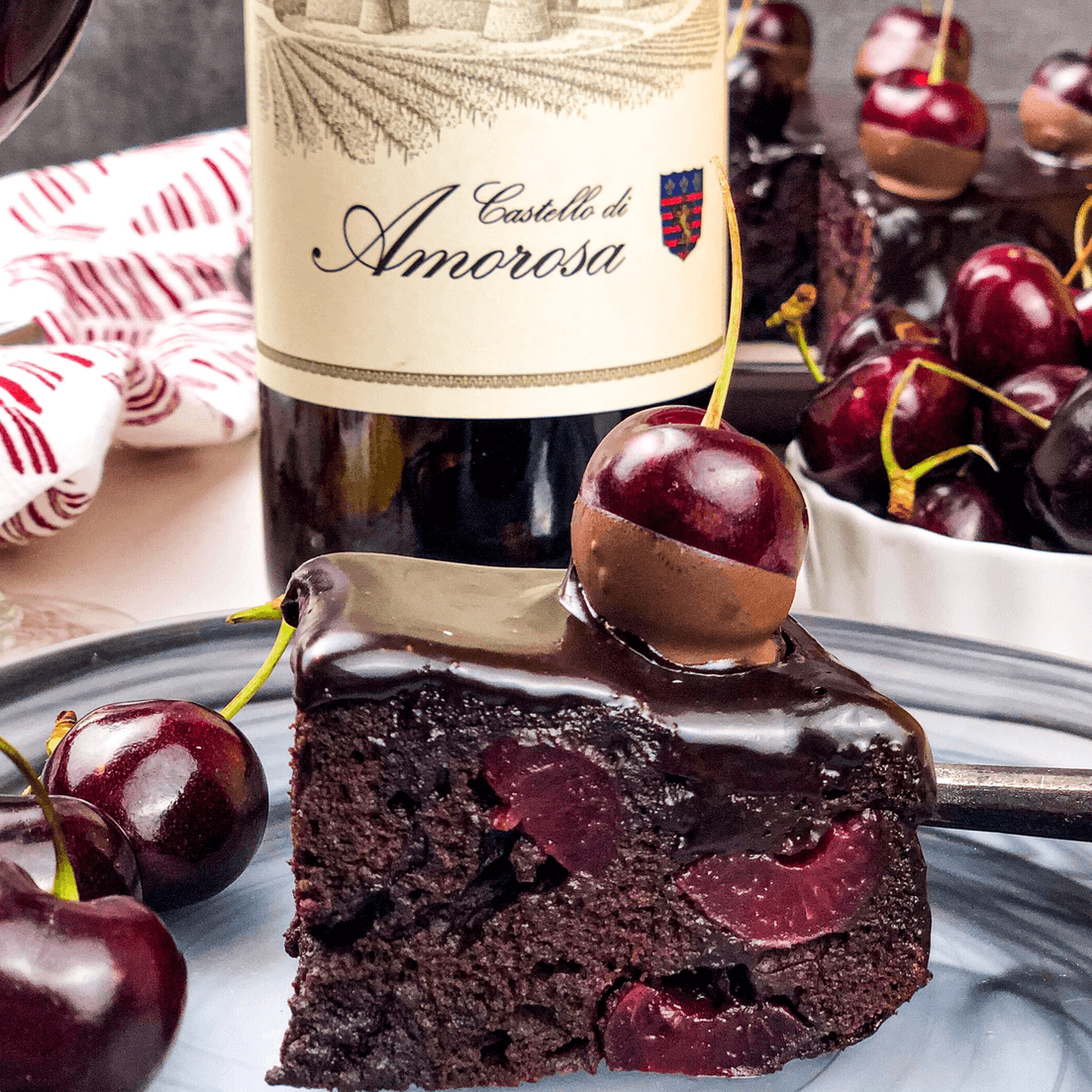 Slice of chocolate cherry cake with a bottle of Castello di Amorosa wine and fresh cherries.