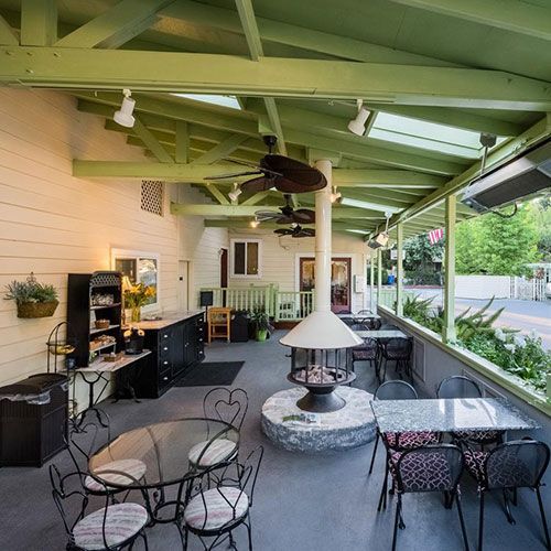 Outdoor dining area with tables and a central fireplace under a green-painted roof.