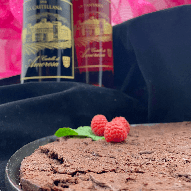 Chocolate cake with raspberries, mint leaf, wine bottles in background.