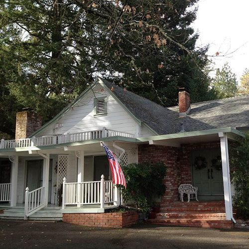 White house with brick accents, porch, American flag, and greenery.