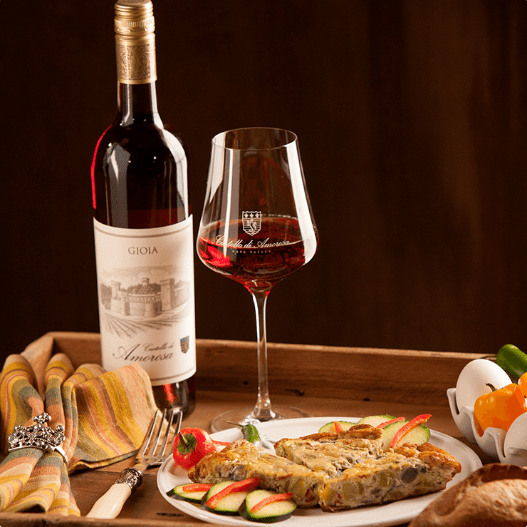 A bottle of Gioia wine, eggs, peppers, and zucchini in a rustic wooden basket.