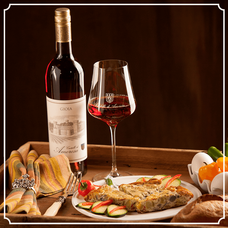 Bottle of red wine, glass of wine, plate of food, and vegetables on a tray.