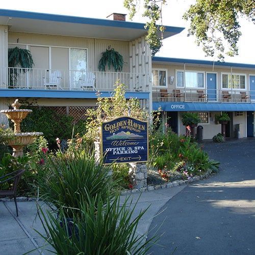 Golden Haven Hot Springs resort exterior with sign, garden, fountain, and motel rooms.