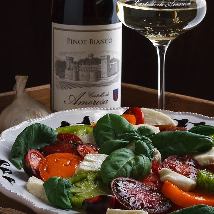 Caprese salad with basil, tomatoes, and mozzarella. Pinot Bianco wine and glass on a wooden tray.