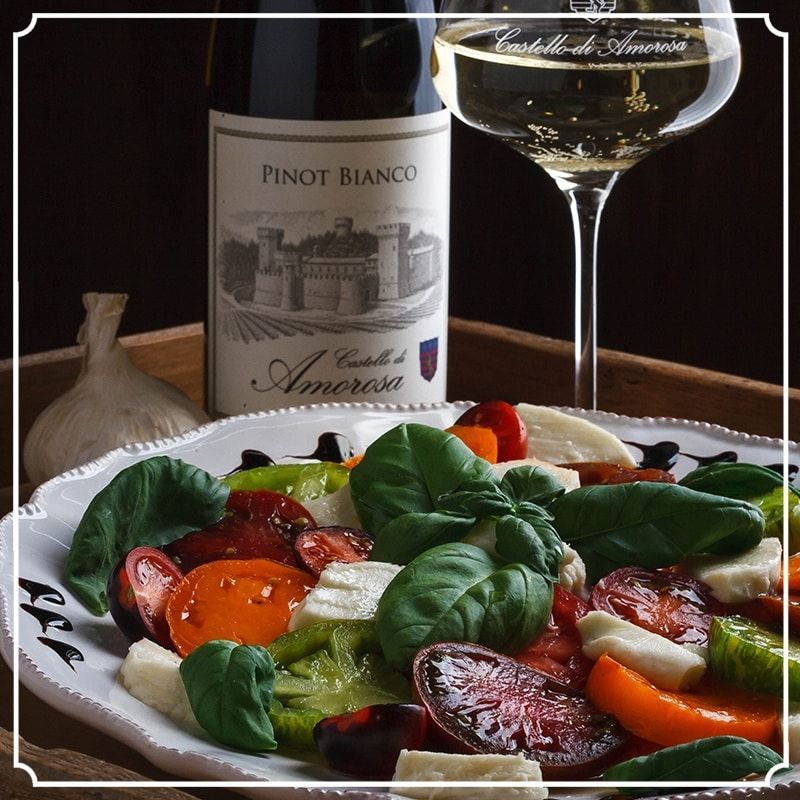 A colorful Caprese salad with a Pinot Bianco bottle and wine glass on a wooden tray.