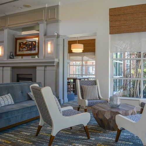 A hotel lobby with seating area; blue sofa, white chairs, wooden coffee table, and large windows.