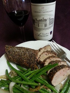 Plate of sliced pork with green beans, onion, and wine; bottle and glass of red wine in background.