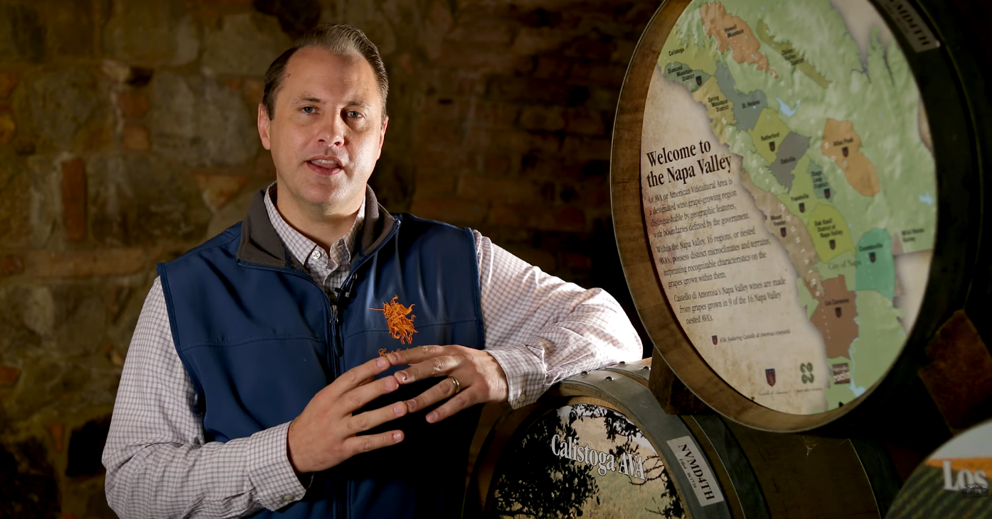 Man in vest speaks near wine barrels, map of Los Carneros AVA.