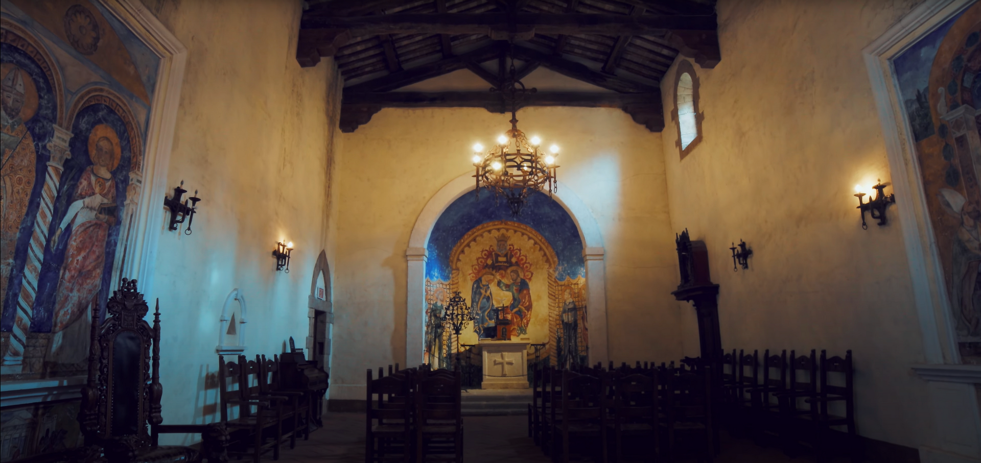 Interior of a church with wooden pews, a chandelier, and a decorated altar. Blue and gold details on the walls.
