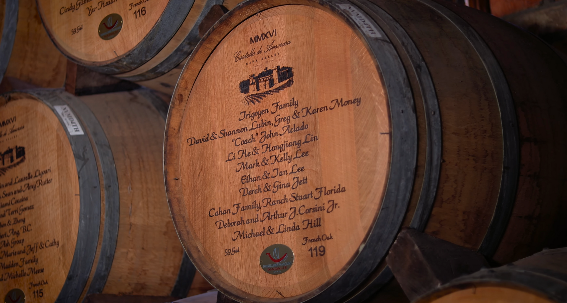 Wooden barrels in a dimly lit room, some with labels and handwritten inscriptions, stacked.