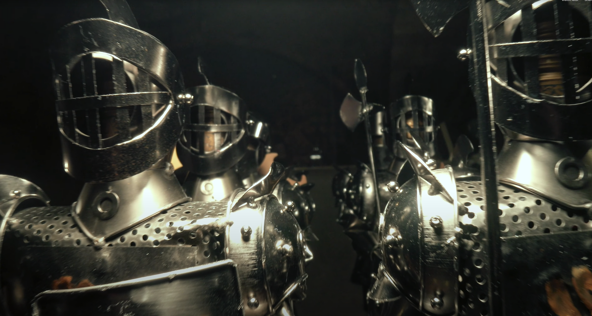Two suits of shiny metal armor in a dark room, reflected in a mirror.