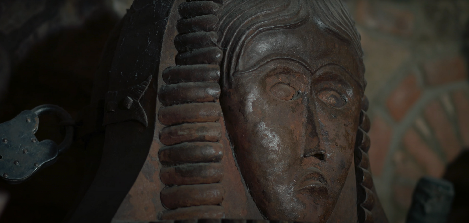 A carved wooden face, possibly a sculpture in a dark setting, details are visible in the aged wood.