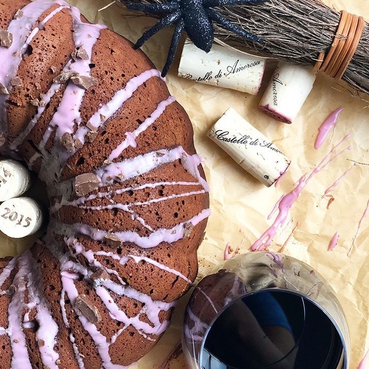Bundt cake with pink glaze, wine glass, corks, spider, and small broom on parchment paper.