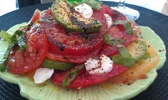 Tomato and avocado salad with mozzarella and basil on a green plate.