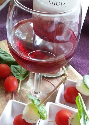 Wine glass near cherry tomatoes, basil, and appetizer skewers