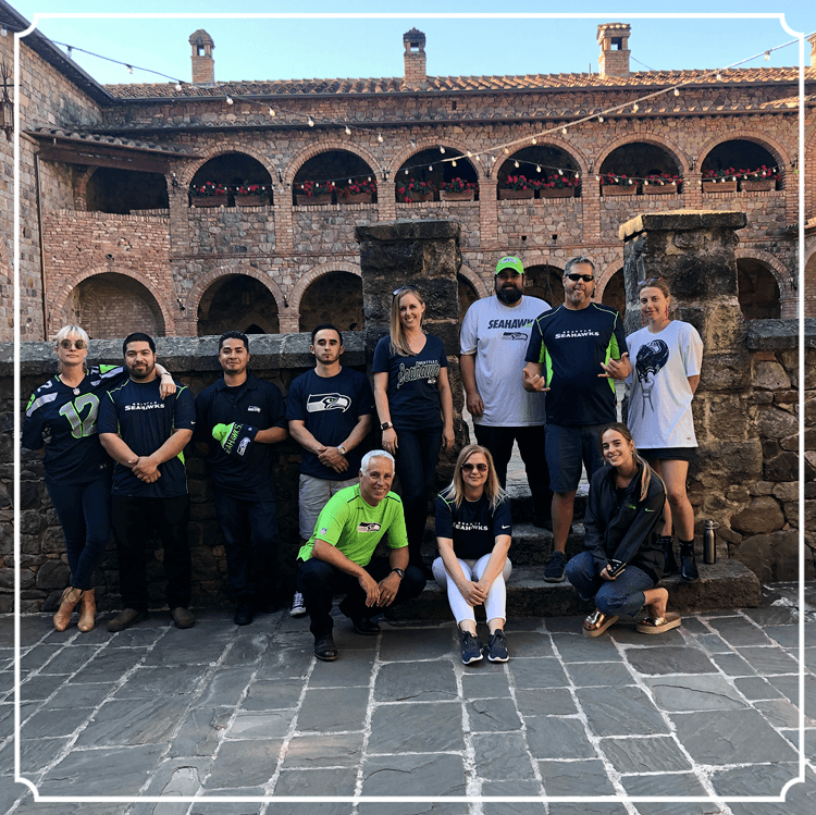 Group of people posing outdoors in front of a brick building with arches.