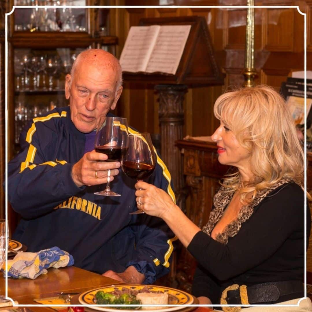Man and woman toasting with red wine at a table. Elaborate wooden dining room.