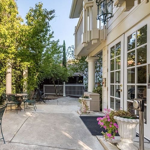 Outdoor patio with white building, French doors, potted flowers, and wrought iron furniture.