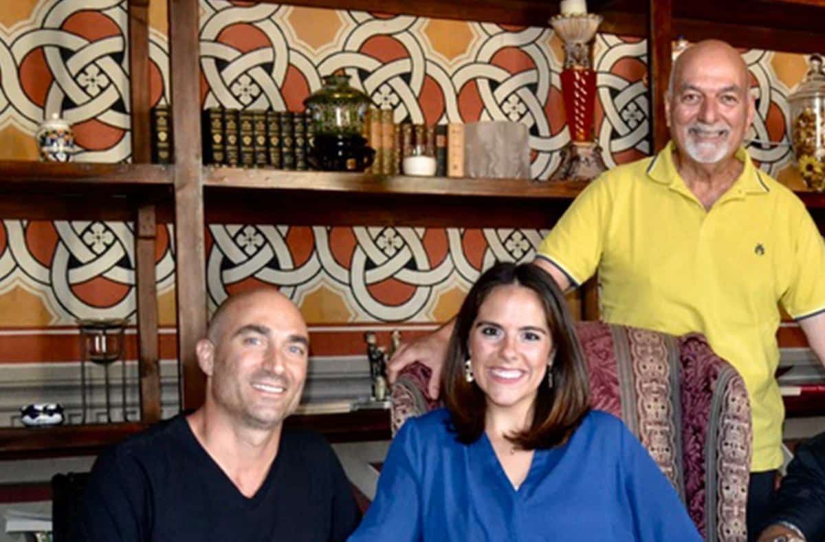 Three people posing. Woman in blue, man in yellow, and man with shaved head. Bookshelf background.