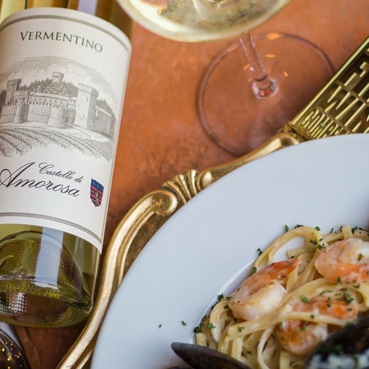 Bottle of white Vermentino wine next to a plate of pasta with shrimp and a gold-rimmed plate.