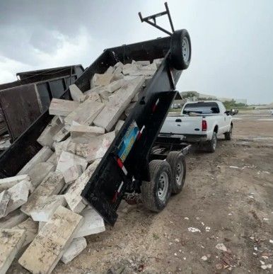 A truck bed being dumped, overflowing with concrete slabs, with a white pickup truck hitched in a dirt area. A truck bed being dumped, overflowing with concrete slabs, with a white pickup truck hitched in a dirt area.