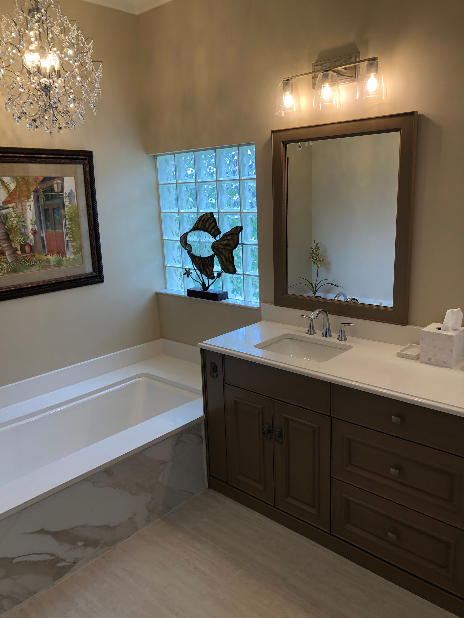 A bathroom with a tub, sink, mirror and chandelier.
