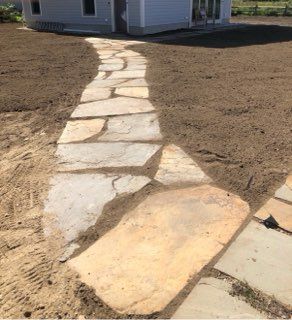 Stone walkway leads across a bare dirt yard to a small building.