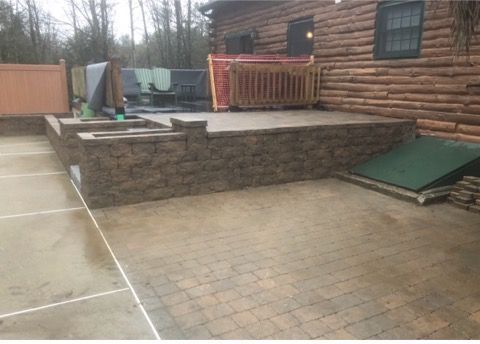 Log cabin patio with stone retaining wall, paved courtyard, and green ramp beside a deck