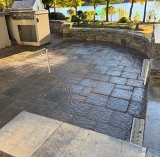 Stone patio with built-in grill, stone wall, and view of trees and water in the background