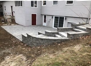 Backyard retaining wall with steps beside a house, featuring stone and concrete terraces.